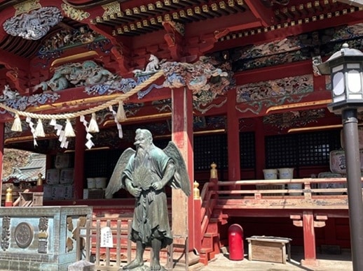朱色の御本社とその前に立つ天狗の石造