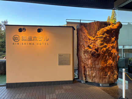 霧島ホテルのエントランスに立つ巨大な屋久杉とホテルロゴの外観写真